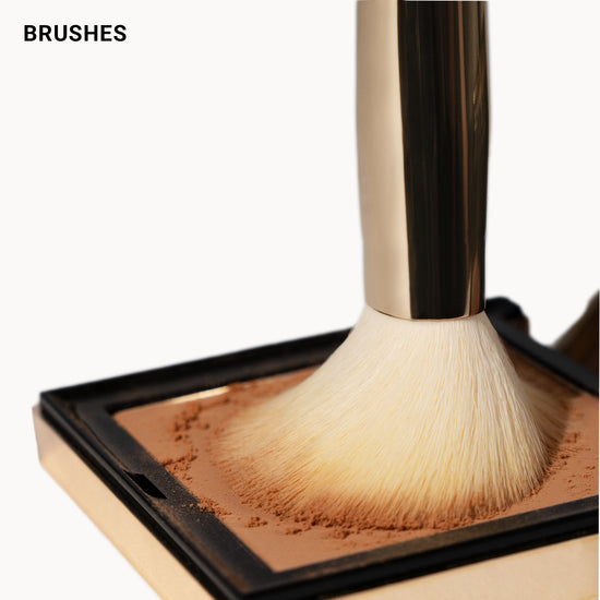 Makeup brush interacting with a compact of powder on a white background