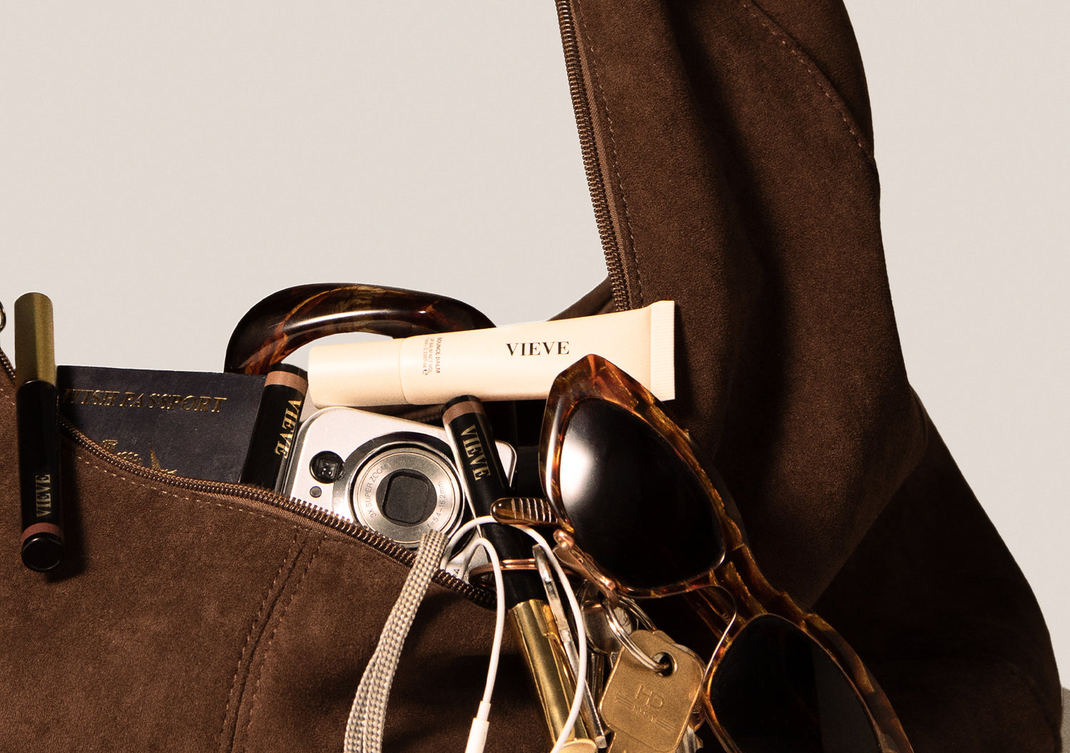 Brown leather bag with sunglasses, camera, and other items on a beige background