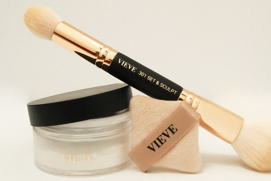 VIEVE 301 Double-Ended Set & Sculpt Brush resting on a jar of Invisiveil Loose Setting Powder, with a diamond-shaped Precision Powder Puff, on a cream background.