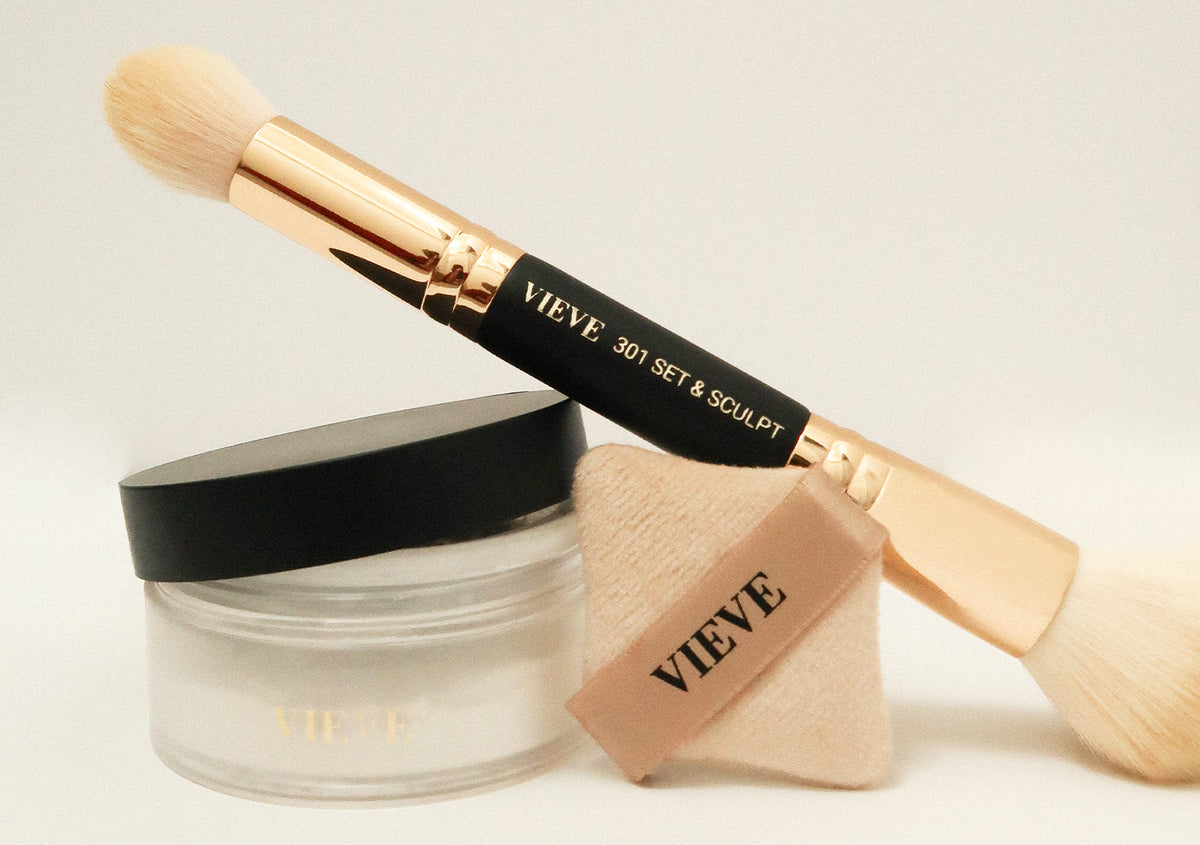 VIEVE 301 Double-Ended Set & Sculpt Brush resting on a jar of Invisiveil Loose Setting Powder, with a diamond-shaped Precision Powder Puff, on a cream background.