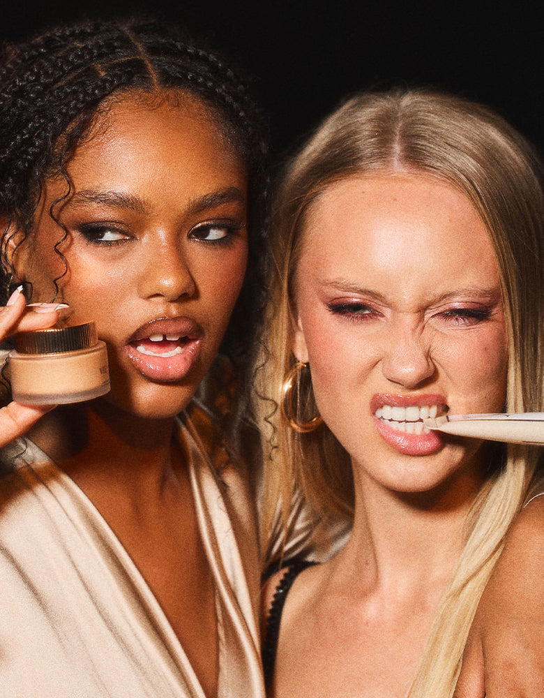 Two models posing playfully against a dark background, one holding a jar of VIEVE Super Skin Nova Moisture Rich Primer and the other biting a tube of Skin Nova Instant Radiance Primer.